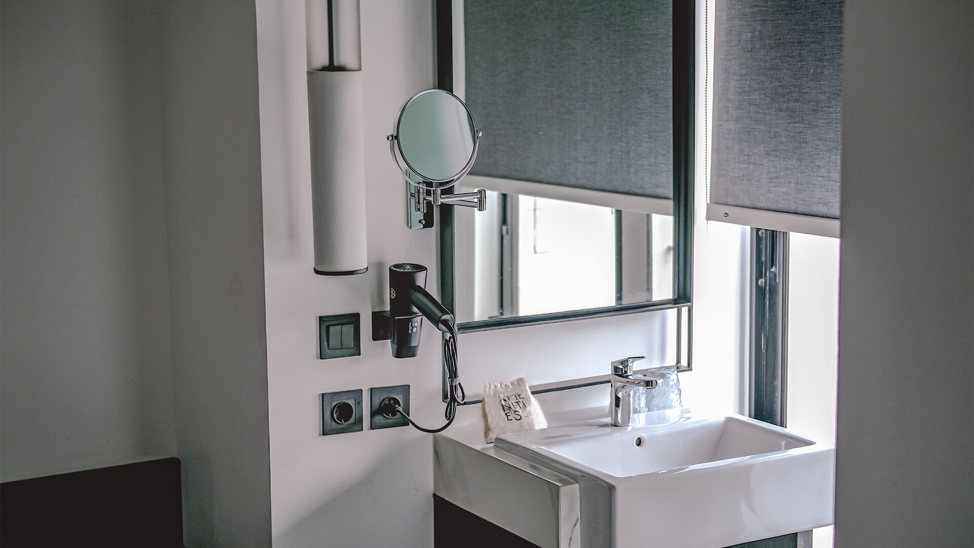 A bathroom with a white sink, a mirror, a hairdryer, and a towel dispenser.