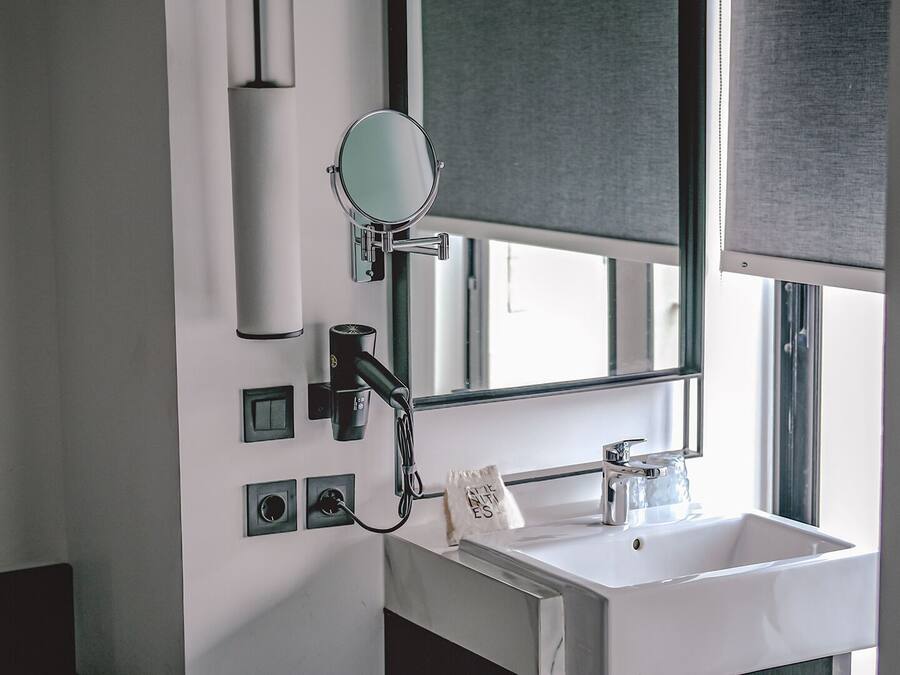 Een badkamer met een wit wastafel, een spiegel, een haardroger en een zeepdispenser.