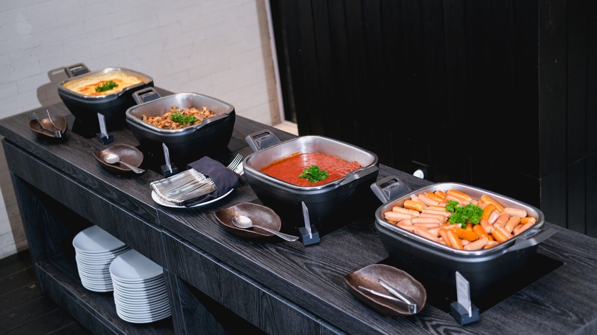 A buffet table with various dishes, including a large pot of soup, a tray of sausages, and several other food items.