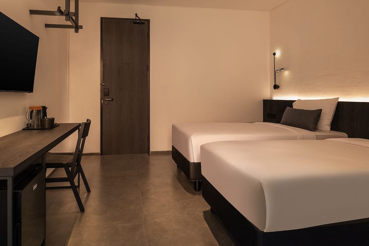 A hotel room with a desk, two beds, a TV, and a door.