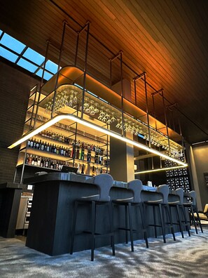 A bar area with multiple shelves of liquor bottles, a bar counter, and bar stools. - REZ Hotel Semarang (Semarang)