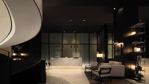 Un moderno vestíbulo de hotel con un mostrador de recepción curvo, zona de estar y una escalera que conduce a un nivel superior.