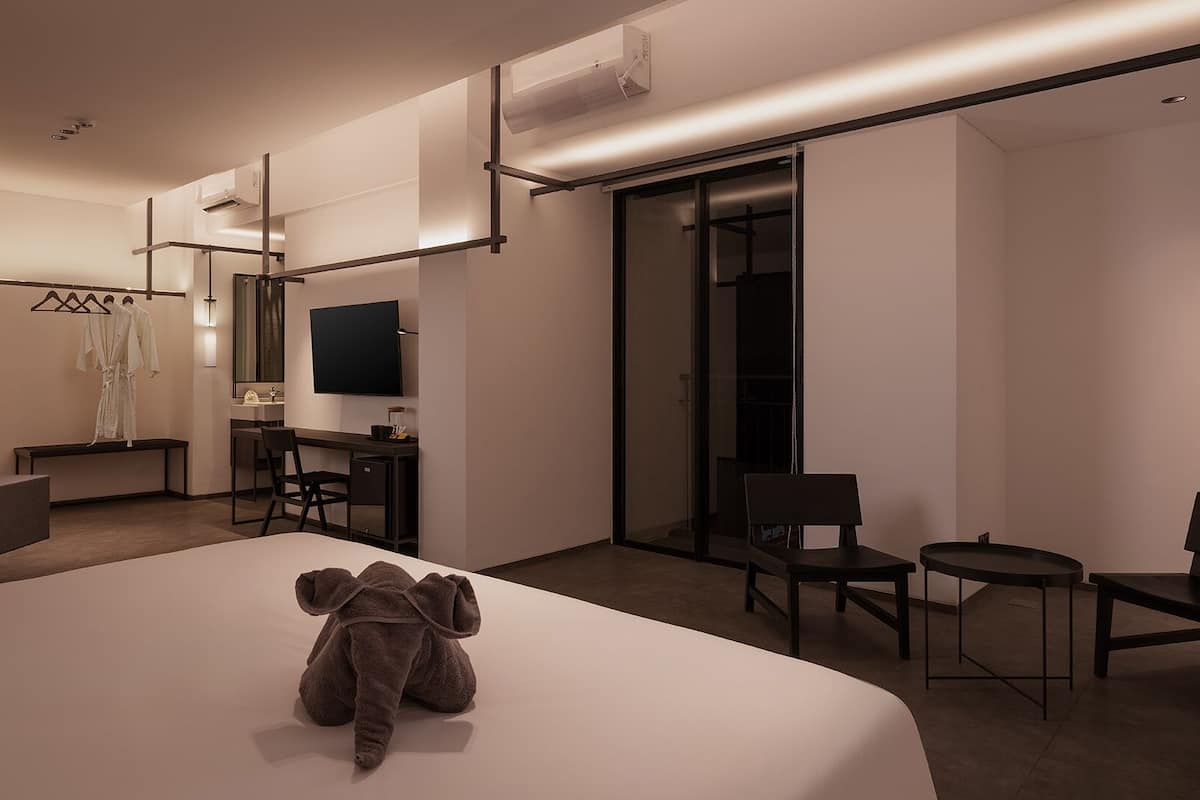 A modern hotel room with a large bed, a desk, a chair, a sofa, and a TV.