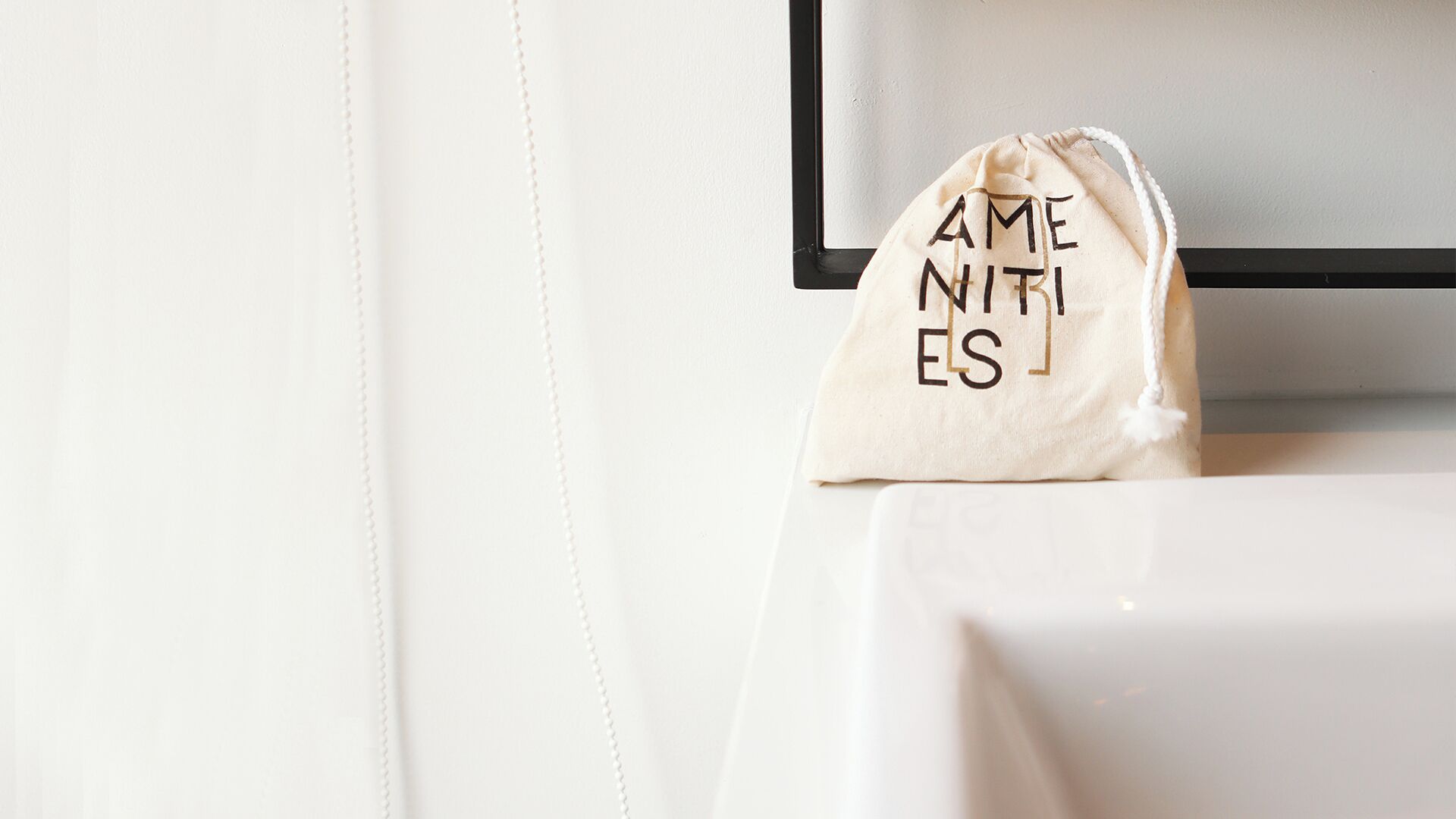 Eine weiße Beutel mit Kordelzug und dem Schriftzug 'AMENITIES' auf weißem Untergrund.