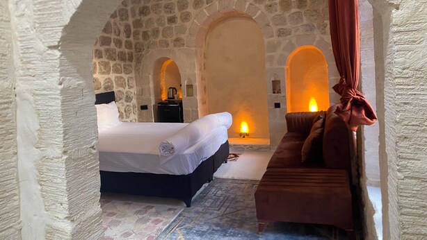 A stone-walled room with a bed, a sofa, and a small table with a kettle. - Roma Konağı Mardin (Mardin)