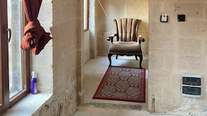 A room with a stone wall, a chair, a red rug, and a window with curtains. - Roma Konağı Mardin (Mardin)