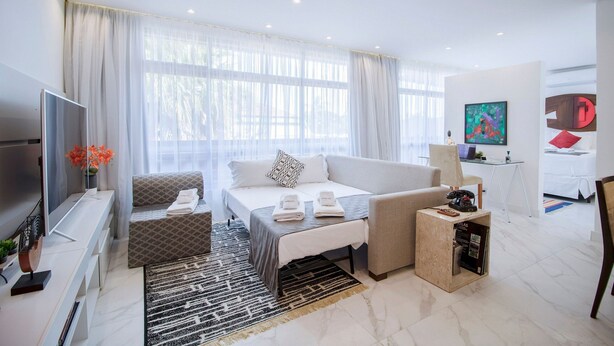 A modern hotel room with a bed, sofa, TV, and a small table with a lamp. - Loft moderno com AC na Praça Pôr do Sol (São Paulo)