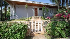 A modern house with a wooden front porch, a stone wall, and a well-maintained garden with various plants and a small staircase leading to the door. - Loft moderno com AC na Praça Pôr do Sol (São Paulo)
