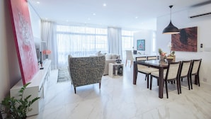 A modern living room with a large TV, a dining area with a table and chairs, and a large window with curtains. - Loft moderno com AC na Praça Pôr do Sol (São Paulo)