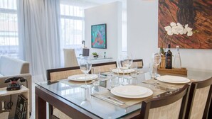 A dining area with a glass table set for four, a modern chandelier, and a painting on the wall. - Loft moderno com AC na Praça Pôr do Sol (São Paulo)