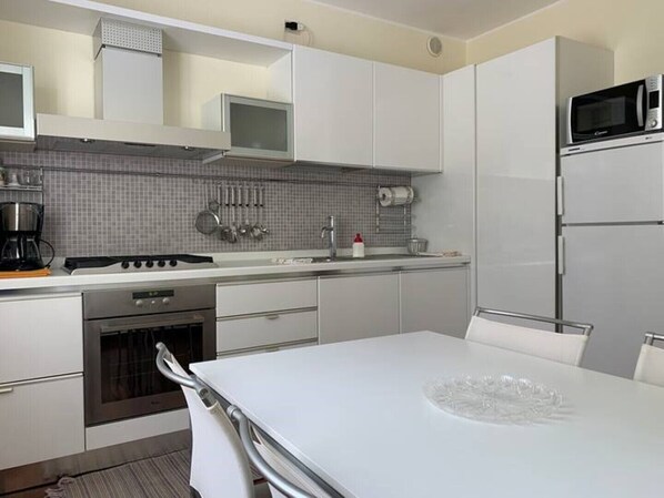A modern kitchen with white cabinets, a stainless steel stove, a microwave, and a sink.