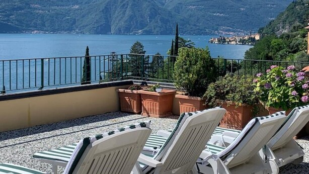 A terrace with lounge chairs overlooking a lake and mountains. - The Terrace on the lake (Fiumelatte)