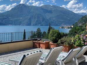 A terrace with lounge chairs overlooking a lake and mountains.
