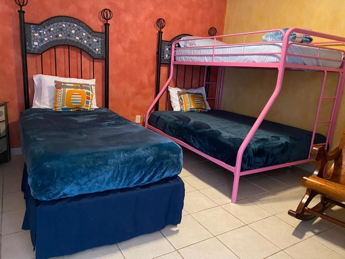 Una habitación con dos literas, una con estructura rosa y otra con estructura negra, ambas con ropa de cama azul.