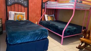 Una habitación con dos literas, una con estructura rosa y otra con estructura negra, ambas con ropa de cama azul.