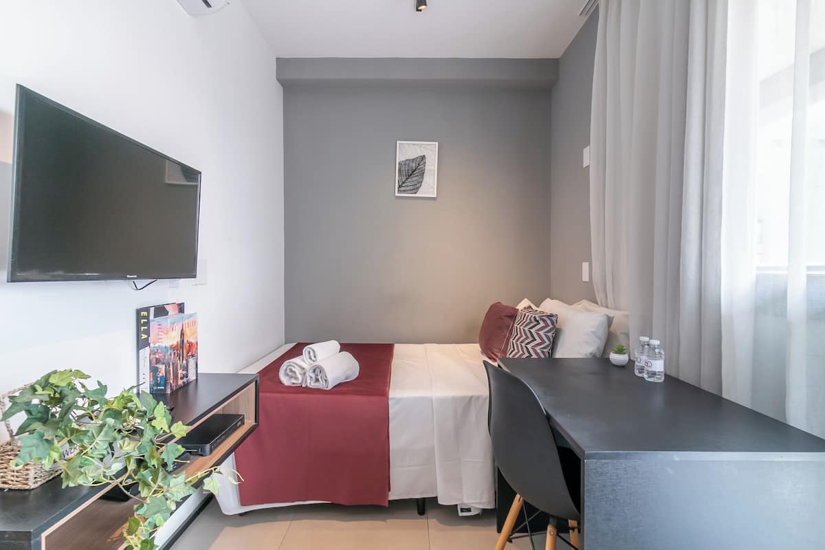 Een moderne hotelkamer met een bed, een bureau, een flatscreen televisie, een plant en een lijst met een afbeelding aan de muur.