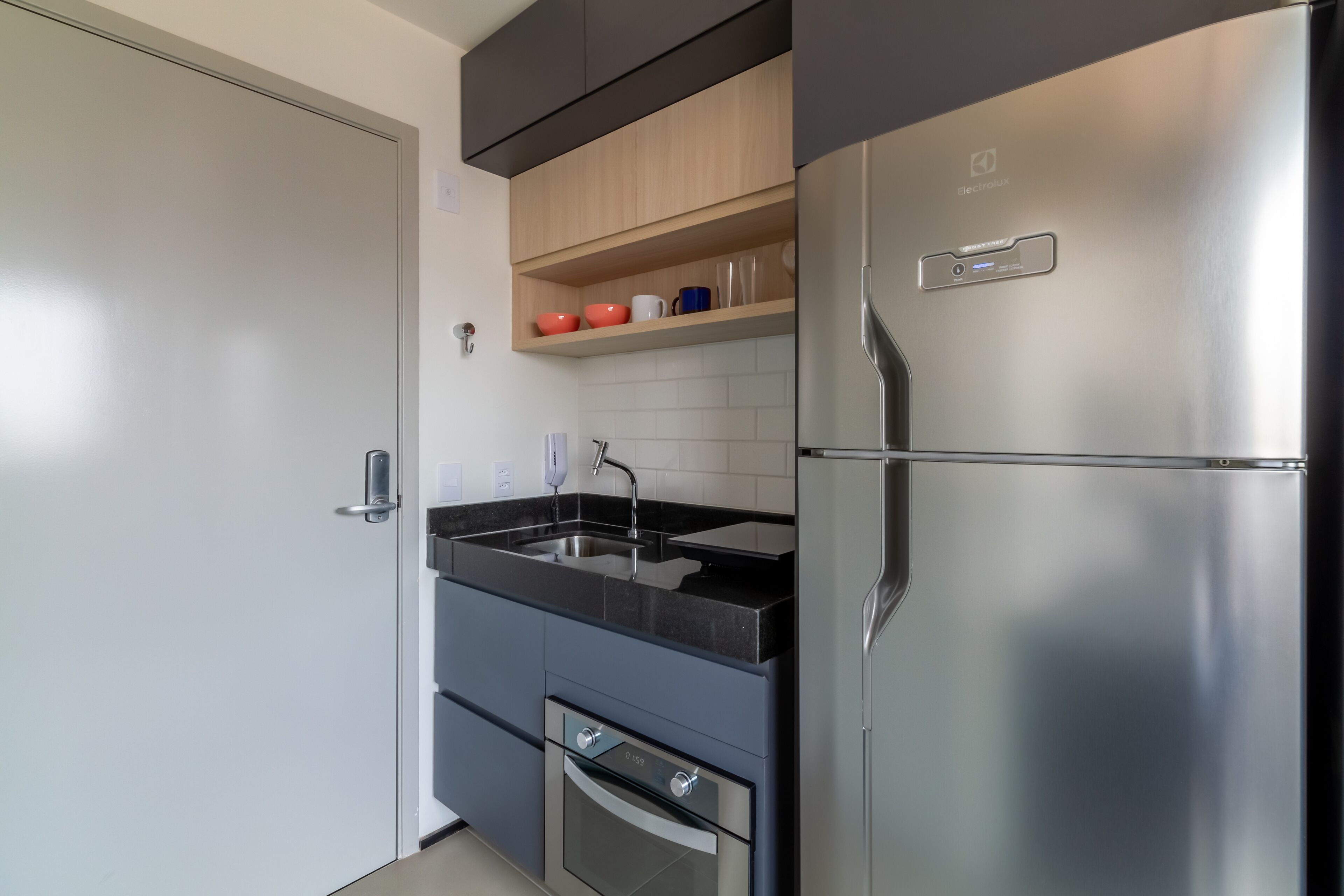 Una cocina moderna con un refrigerador de acero inoxidable, una encimera negra y armarios de madera.