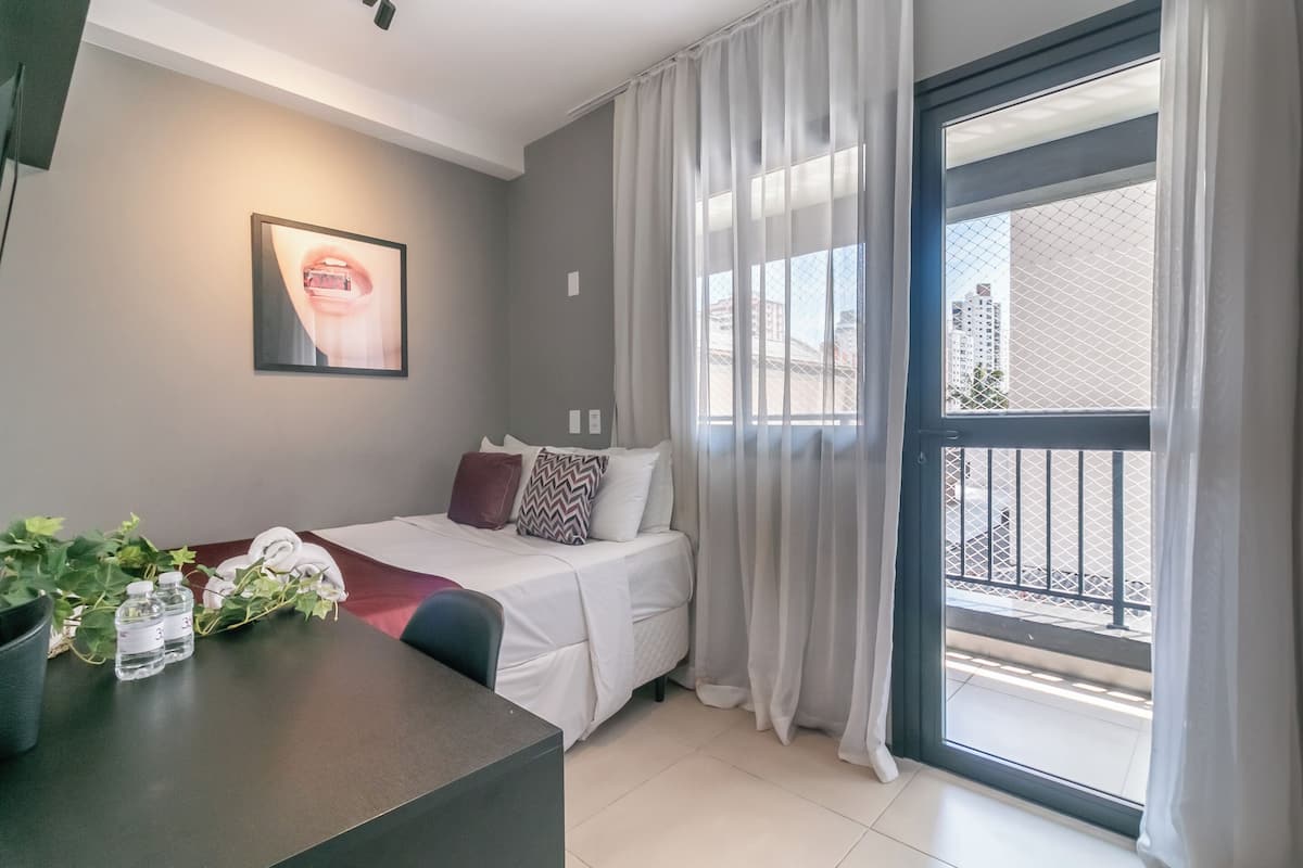 Een moderne hotelkamer met een bed, een bureau, een potplant en een raam met uitzicht op gebouwen.