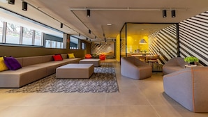 A modern living room with a sofa, ottoman, and chairs, a kitchen area with a counter and stools, and a large window providing natural light. - 360 VN Humberto (São Paulo)