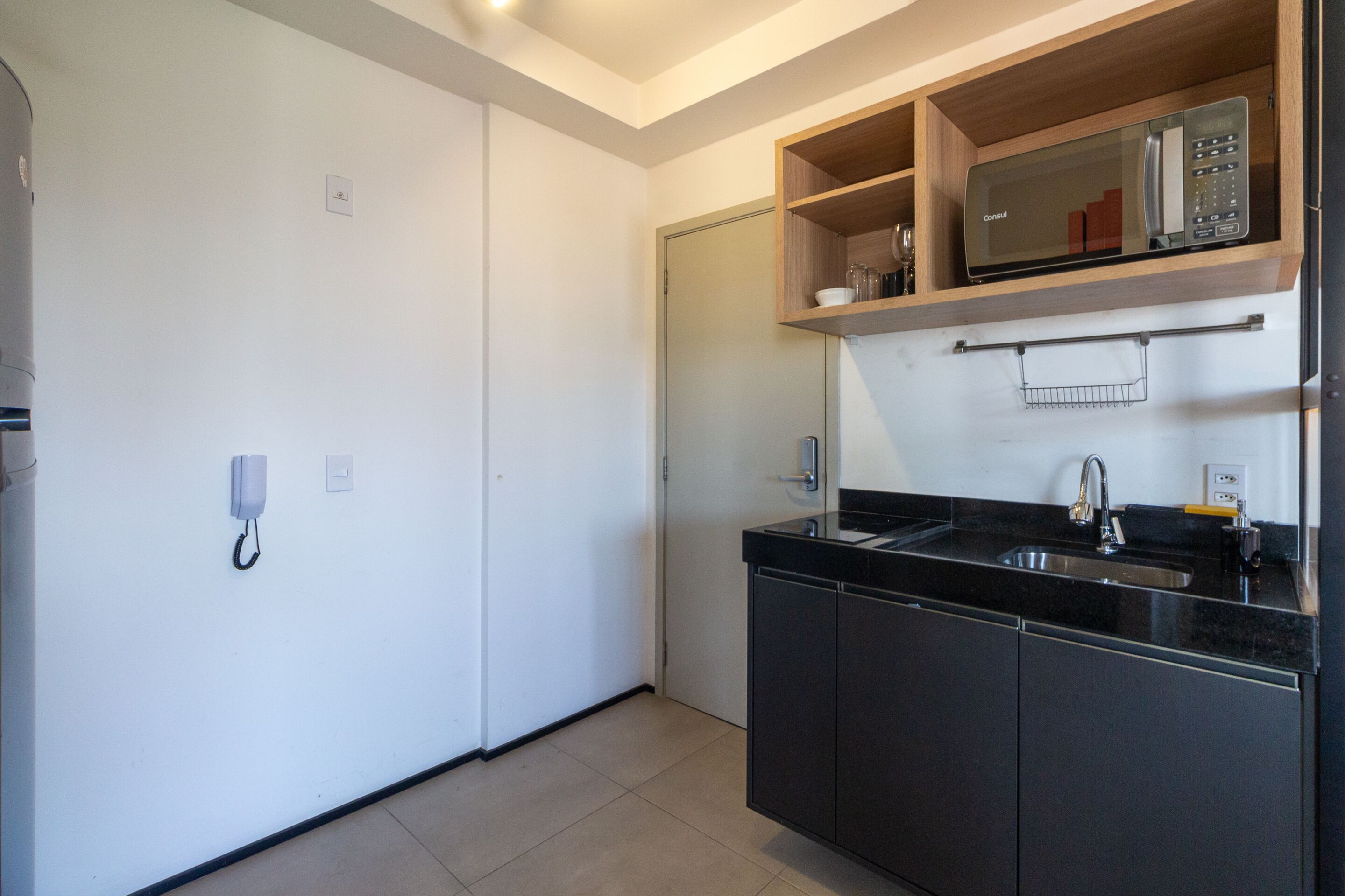 A modern kitchen with a built-in microwave, a black countertop, and a sink.