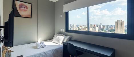 A modern bedroom with a bed, a desk, and a large window offering a city view.