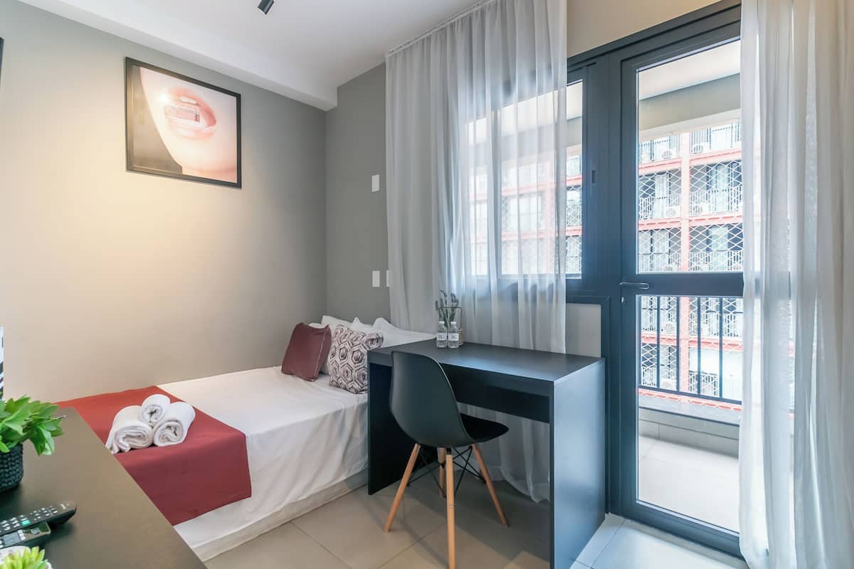 Een hotelkamer met een bed, bureau, stoel en een balkon met uitzicht.