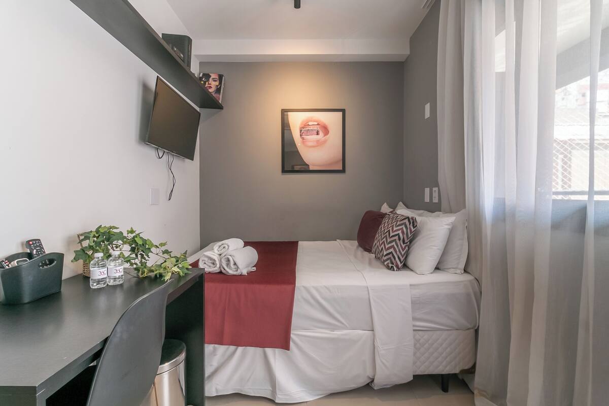 Een moderne slaapkamer met een bed, een bureau, een televisie en een ingelijst beeld aan de muur.