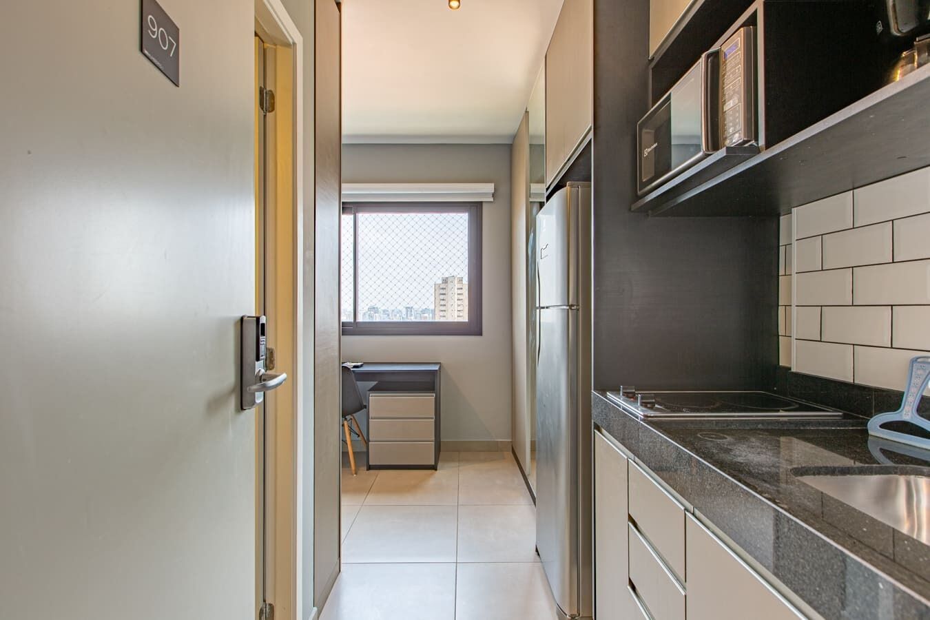 A compact kitchen with a refrigerator, microwave, and a small window.