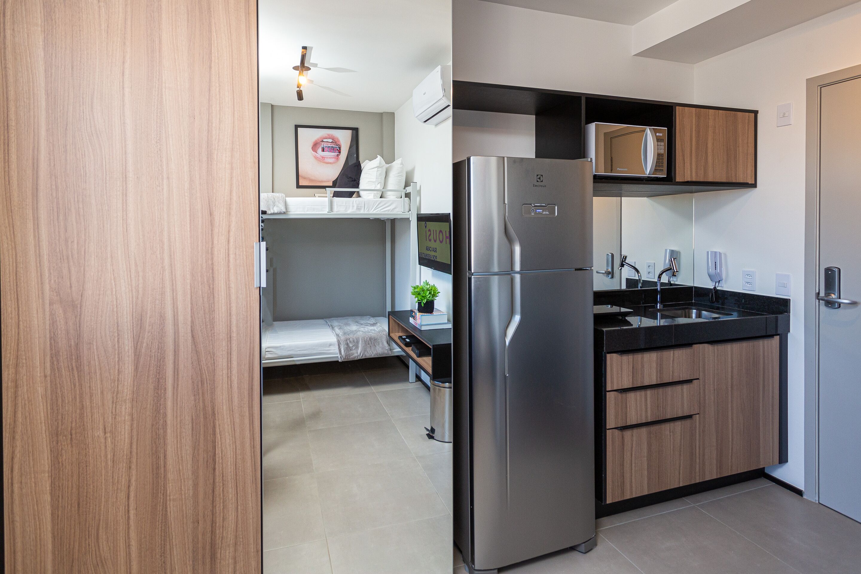 A compact kitchen with a built-in microwave, stainless steel refrigerator, and wooden cabinets.