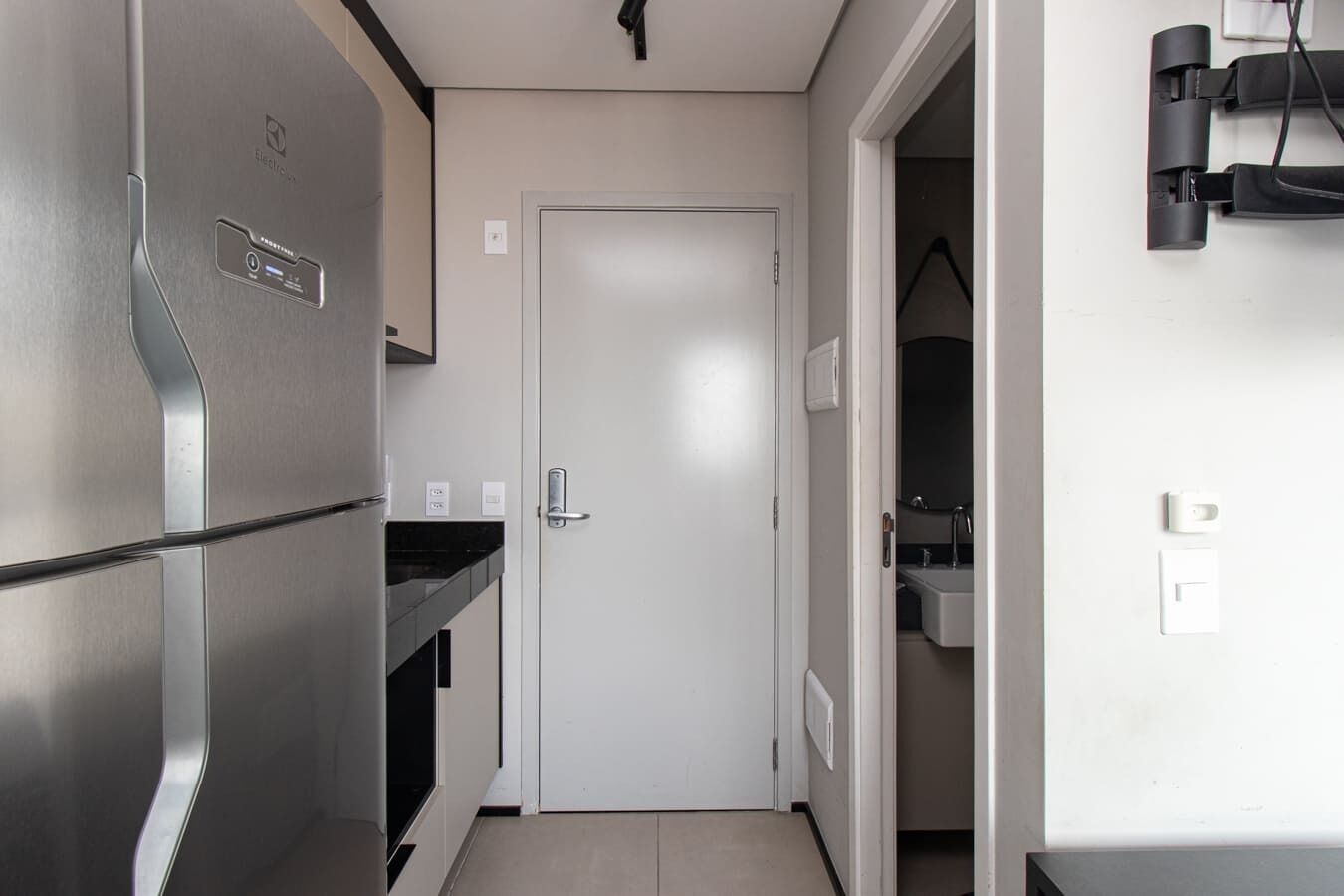 Una cocina estrecha con un refrigerador de acero inoxidable, una puerta blanca y una pequeña encimera.
