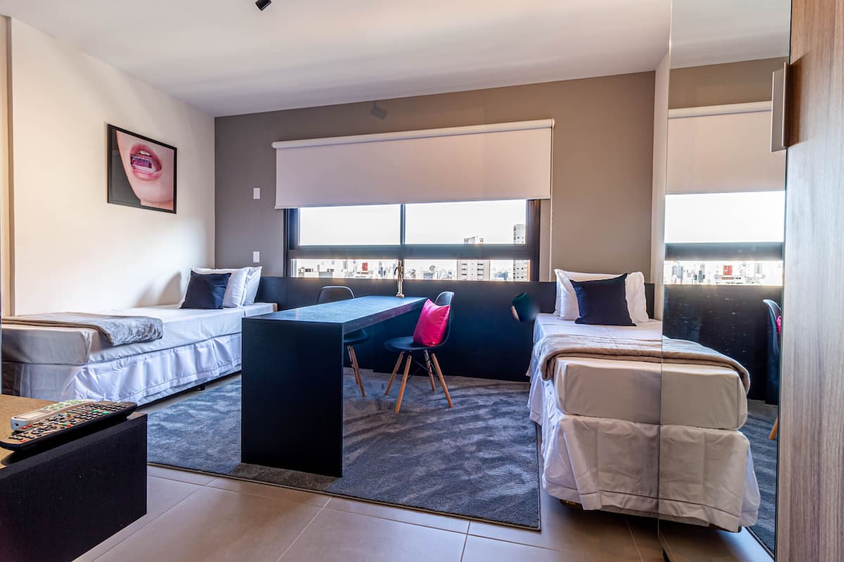 Een moderne hotelkamer met een bed, een bureau en een stoel. Er is een raam met uitzicht op gebouwen.