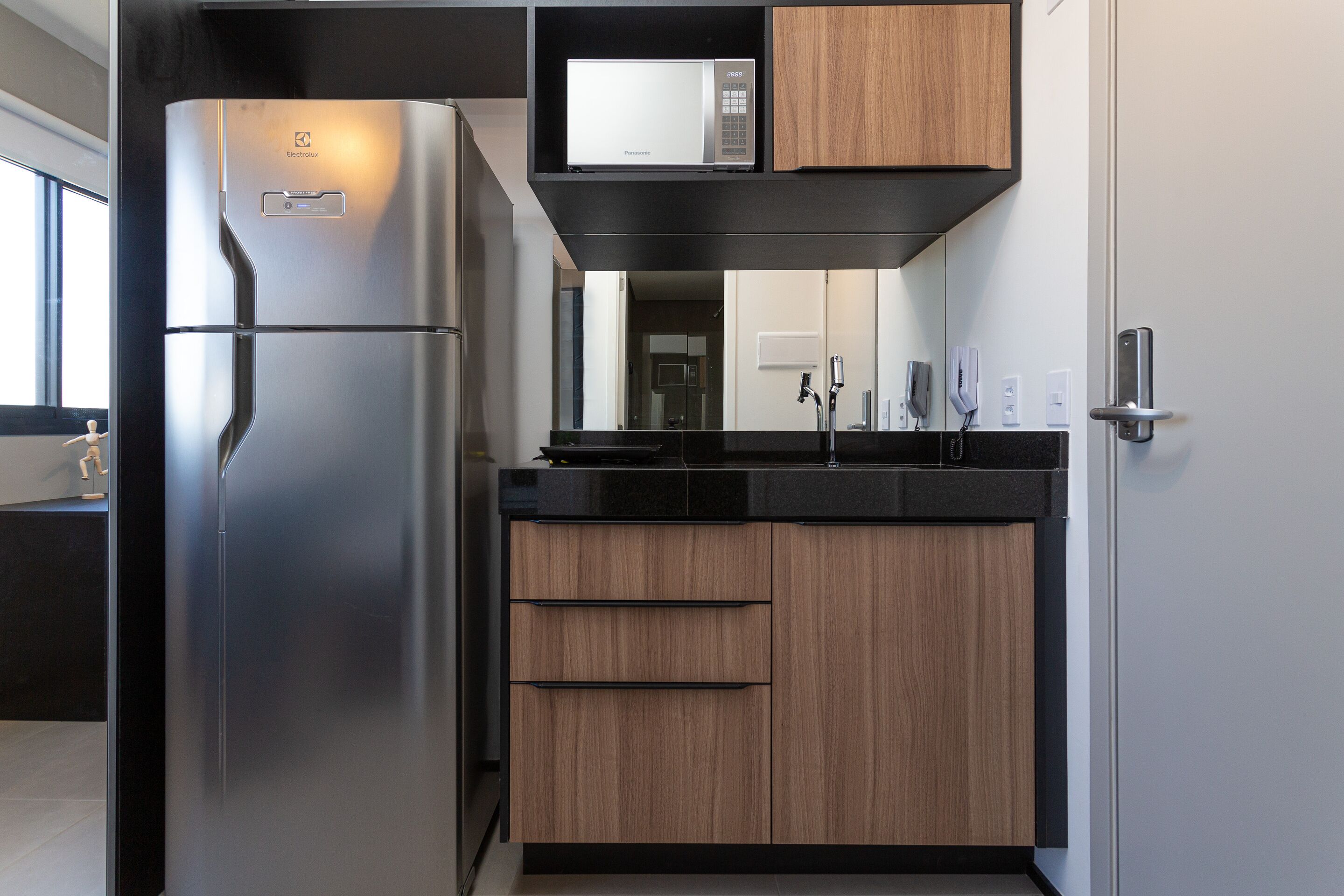 A modern kitchen with a stainless steel refrigerator, wooden cabinets, a black countertop, and a built-in microwave.
