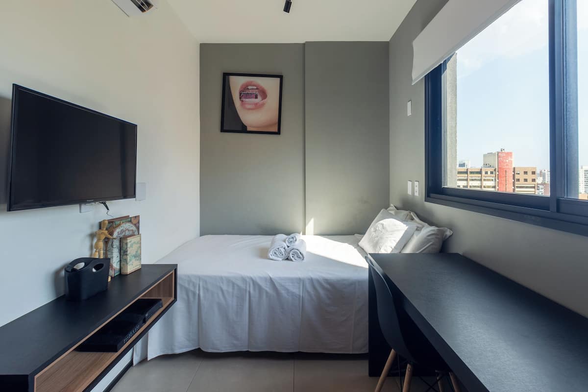 Een moderne hotelkamer met een bed, een bureau, een televisie en een raam met uitzicht op de stad.