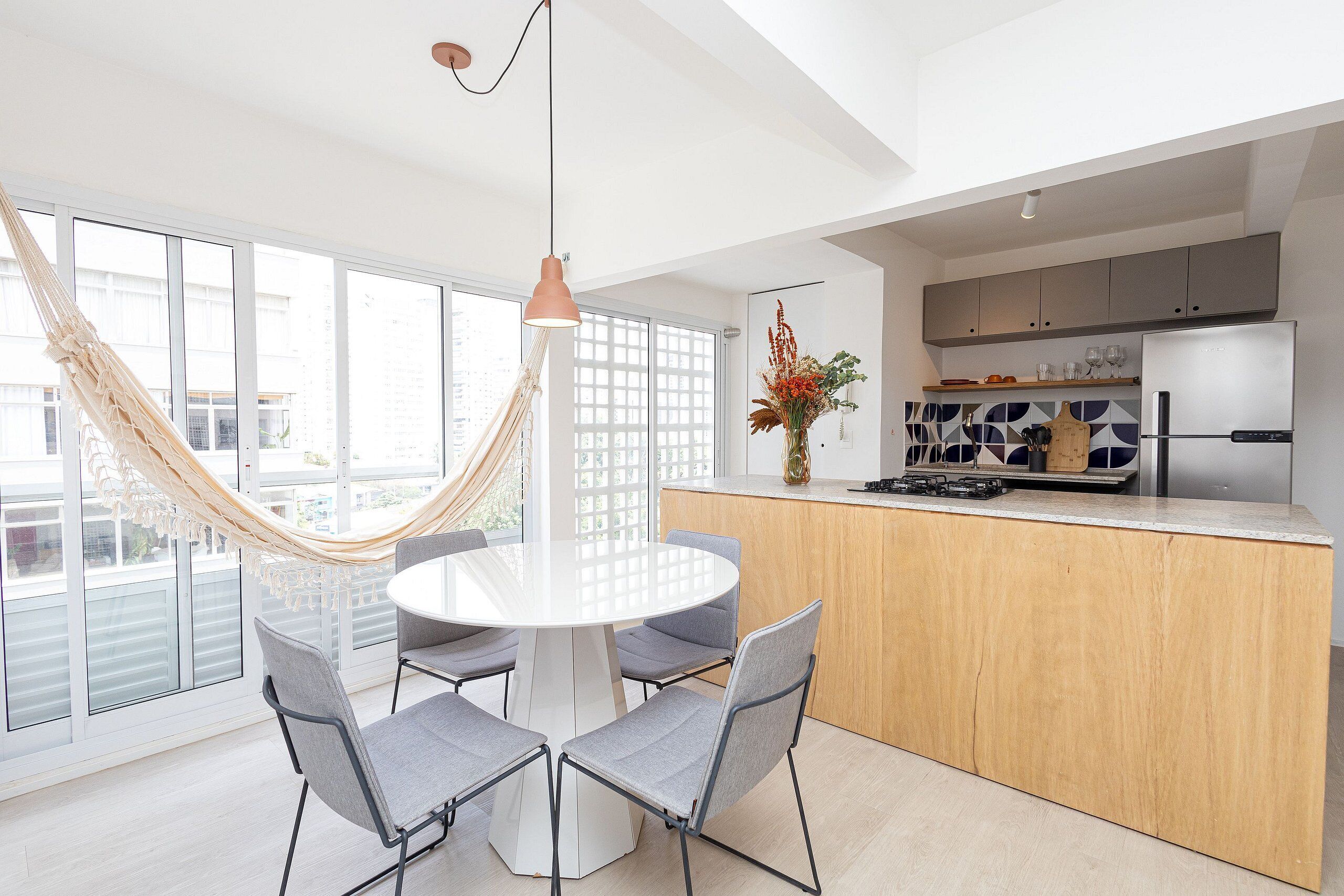 A modern kitchen with a central island, a dining area with a round table and chairs, and a large window with a view of the city.