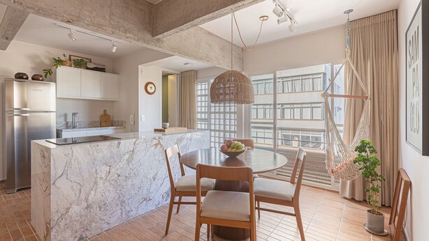 A modern kitchen with a marble island, wooden chairs, and a dining table. - Vossa Bossa Jardins (São Paulo)