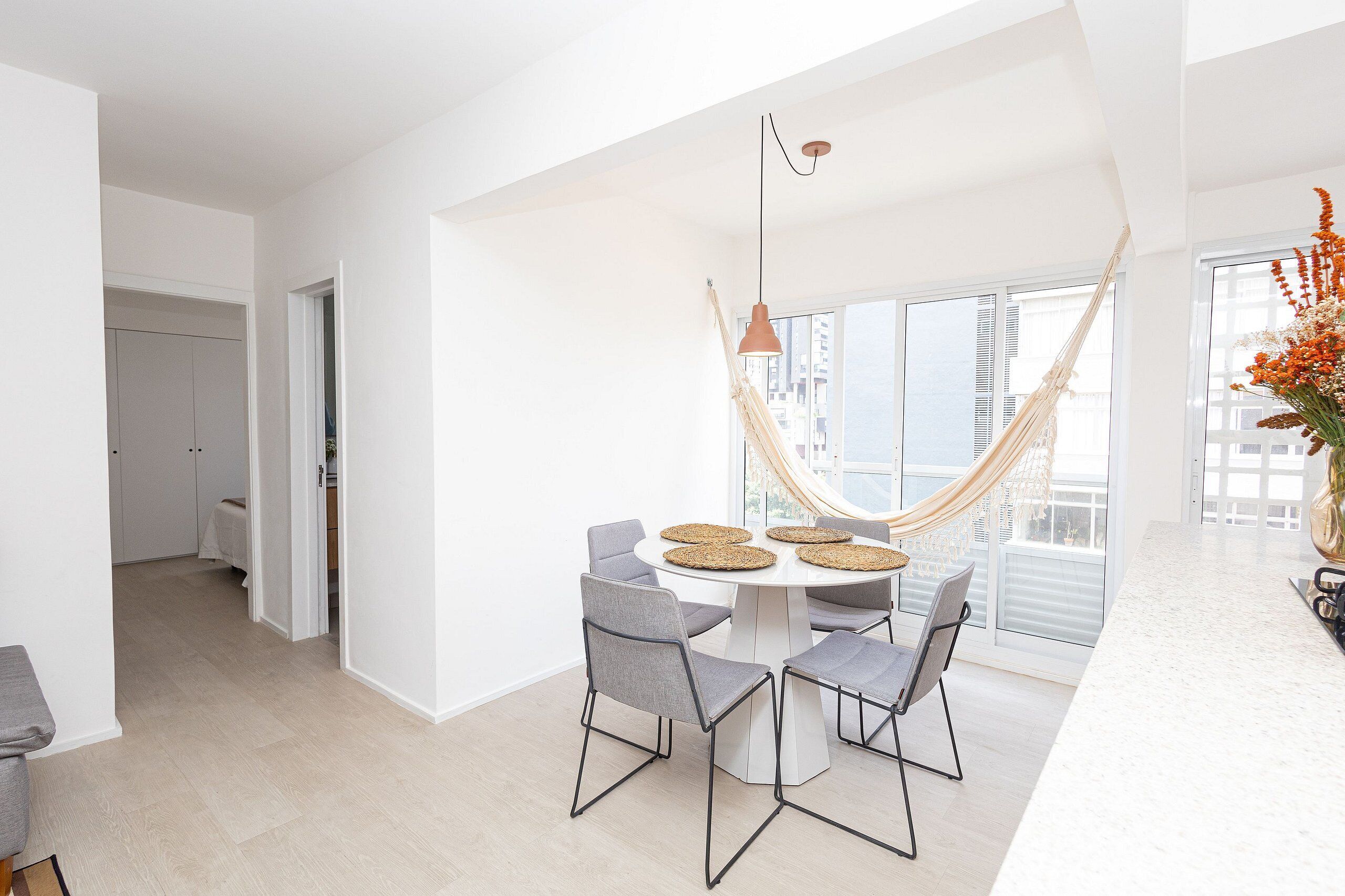 A modern kitchen with a round dining table, grey chairs, and a hanging hammock.