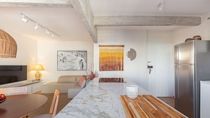 A modern kitchen with a marble countertop, wooden cutting board, stainless steel refrigerator, and a dining area with a table and chairs. - Vossa Bossa Jardins (São Paulo)