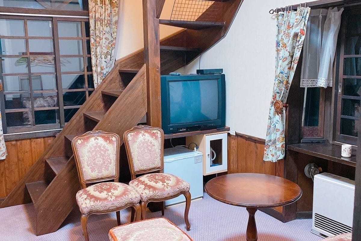 A cozy living room with a wooden staircase, a television, and floral-patterned furniture.
