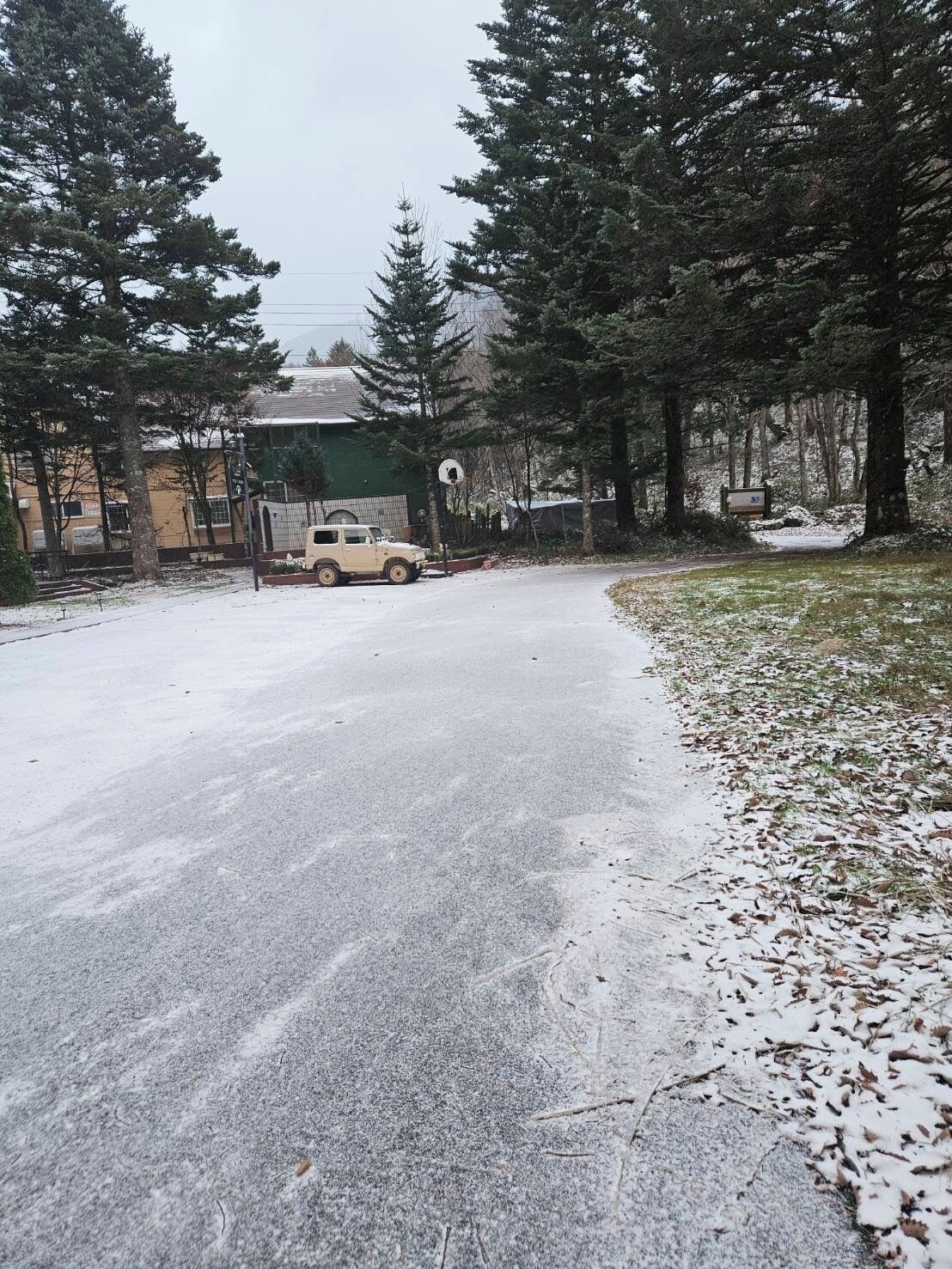 A snow-covered road with a parked vehicle and a building in the background.