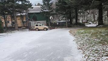 A snow-covered road with a parked vehicle and a building in the background.