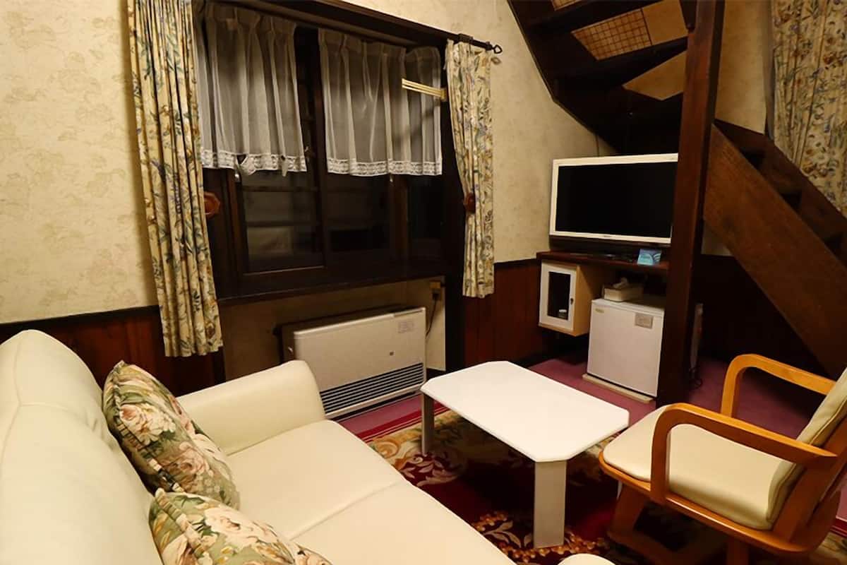 A cozy room with a sofa, a small table, a wooden chair, a television, and a refrigerator.