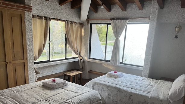 A room with two beds, wooden furniture, and large windows with curtains. - Casa en Club de Golf (Tequisquiapan)