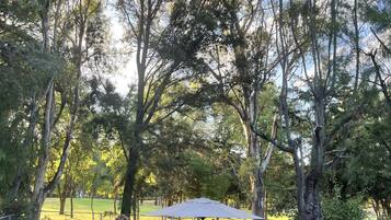 An outdoor seating area with a table and chairs under a canopy, surrounded by trees.