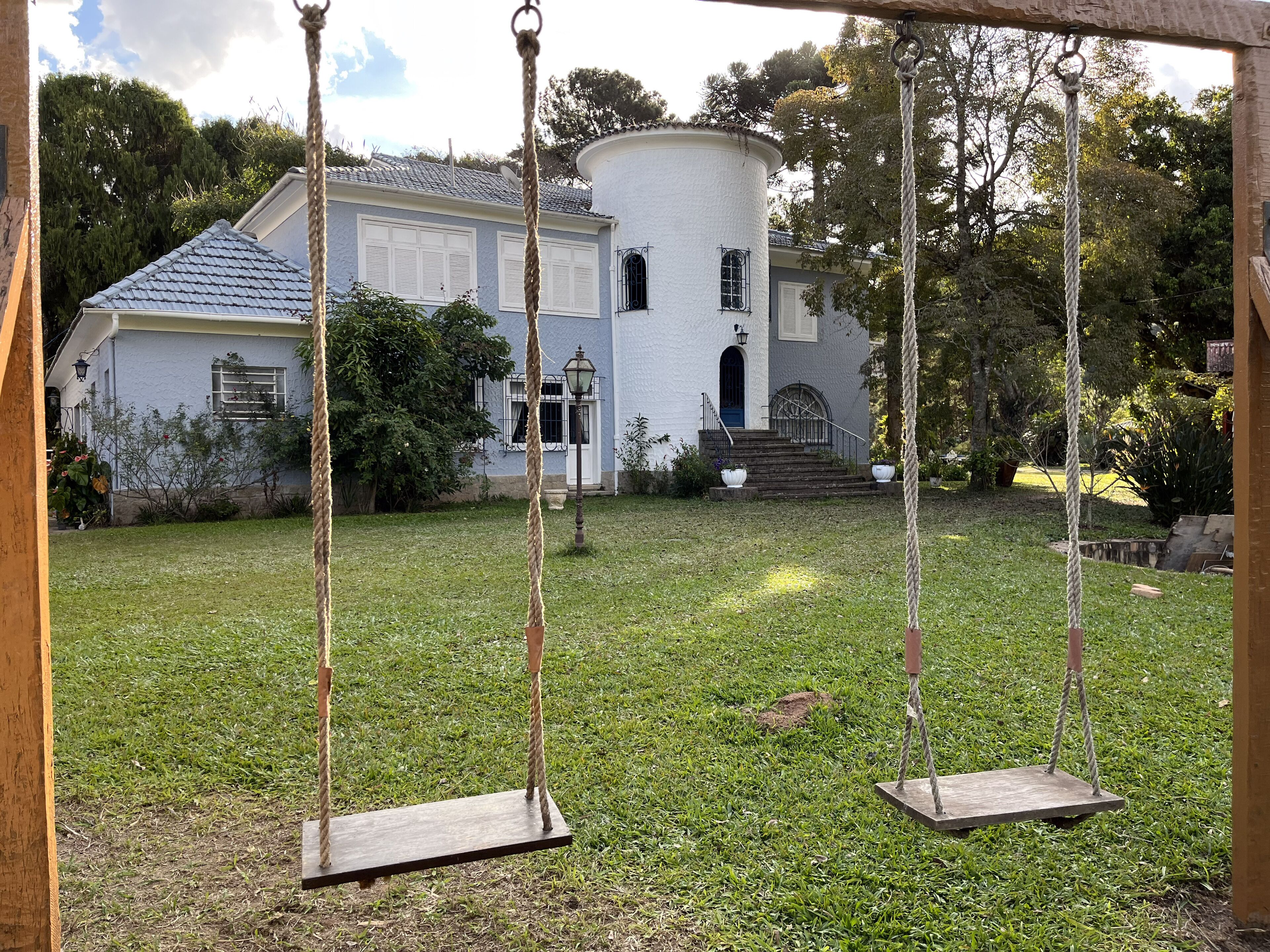 Uma casa branca com porta azul e torre redonda, cercada por um gramado com balanço.