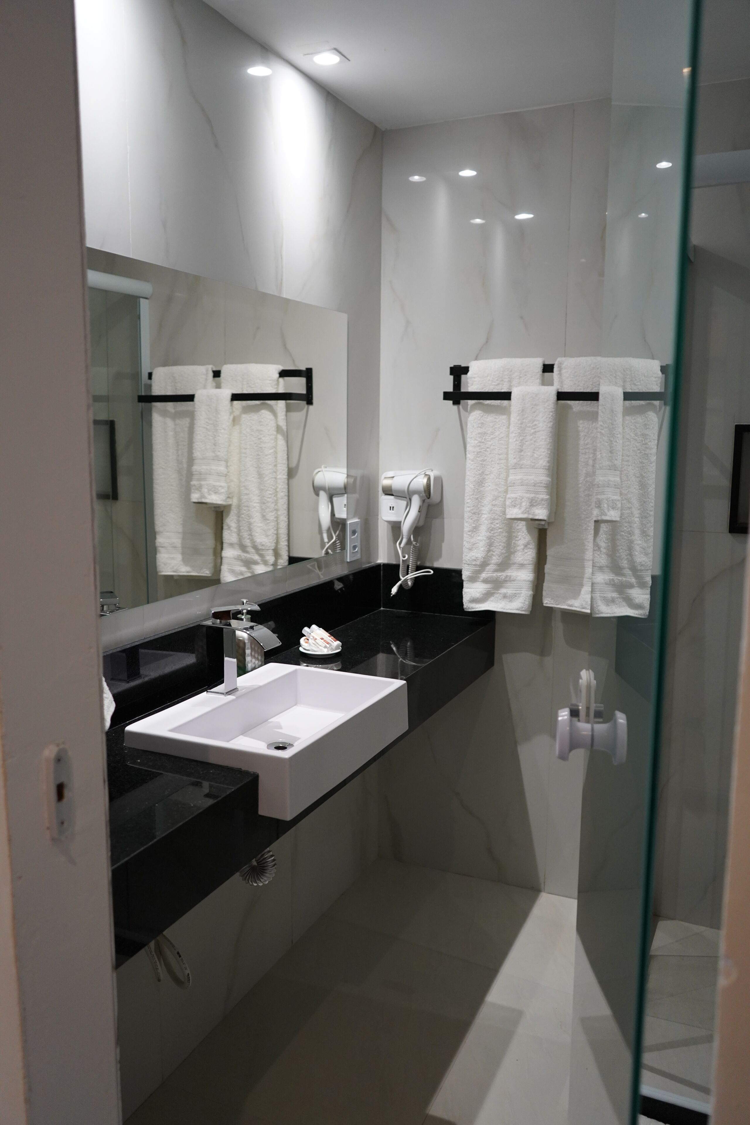 A modern bathroom with a black countertop, white sink, and a glass shower enclosure.