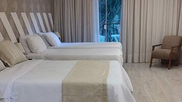 A modern hotel room with two beds, a large window with curtains, a wooden floor, and a ceiling with recessed lighting.
