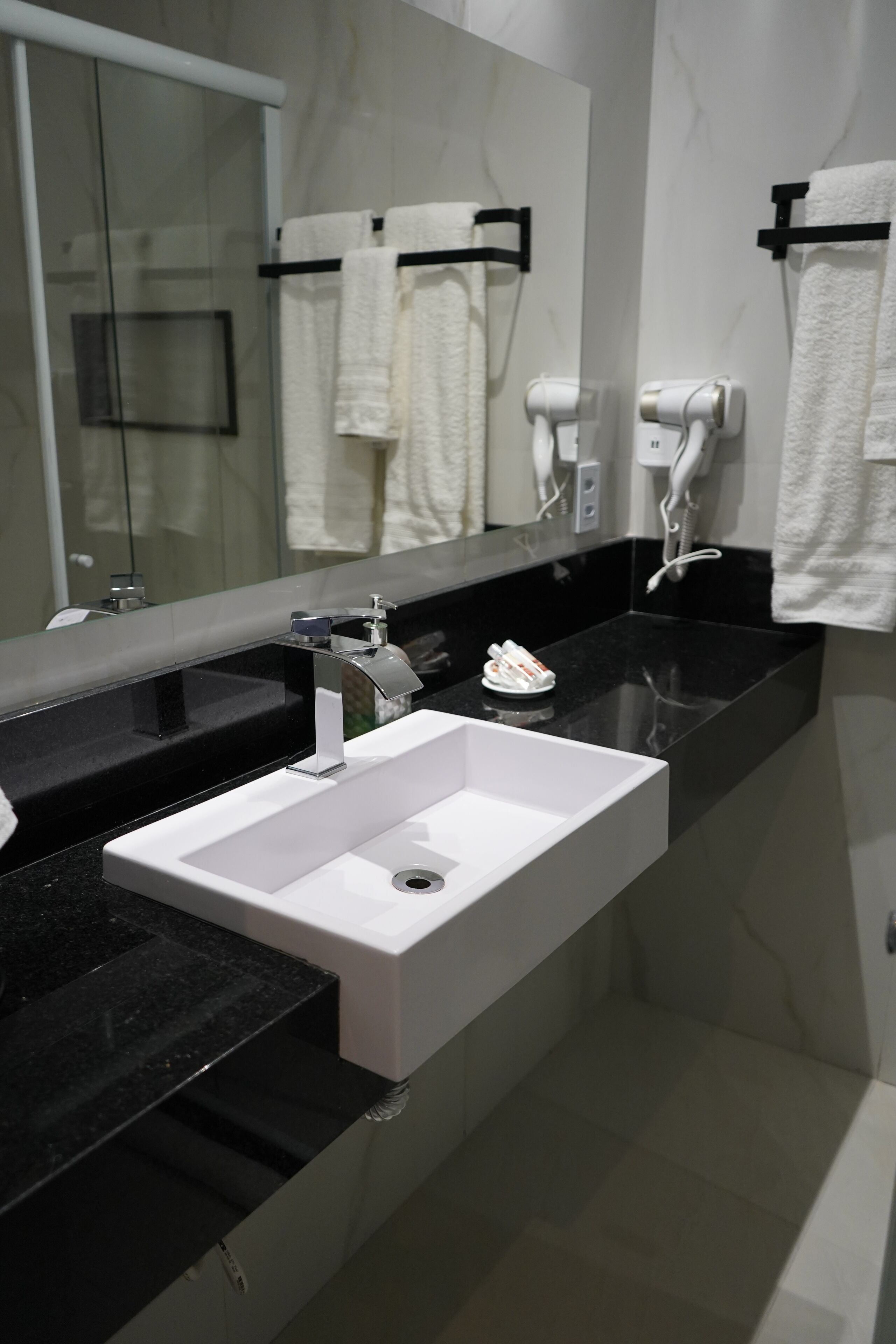 A modern bathroom with a white sink, black countertop, and a large mirror.
