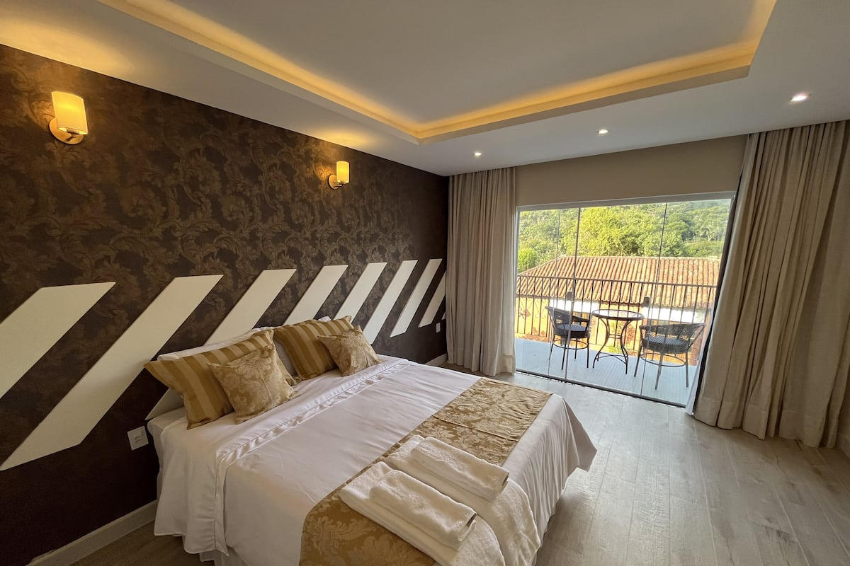 A bedroom with a large bed, a view of the outdoors, and a balcony with chairs.