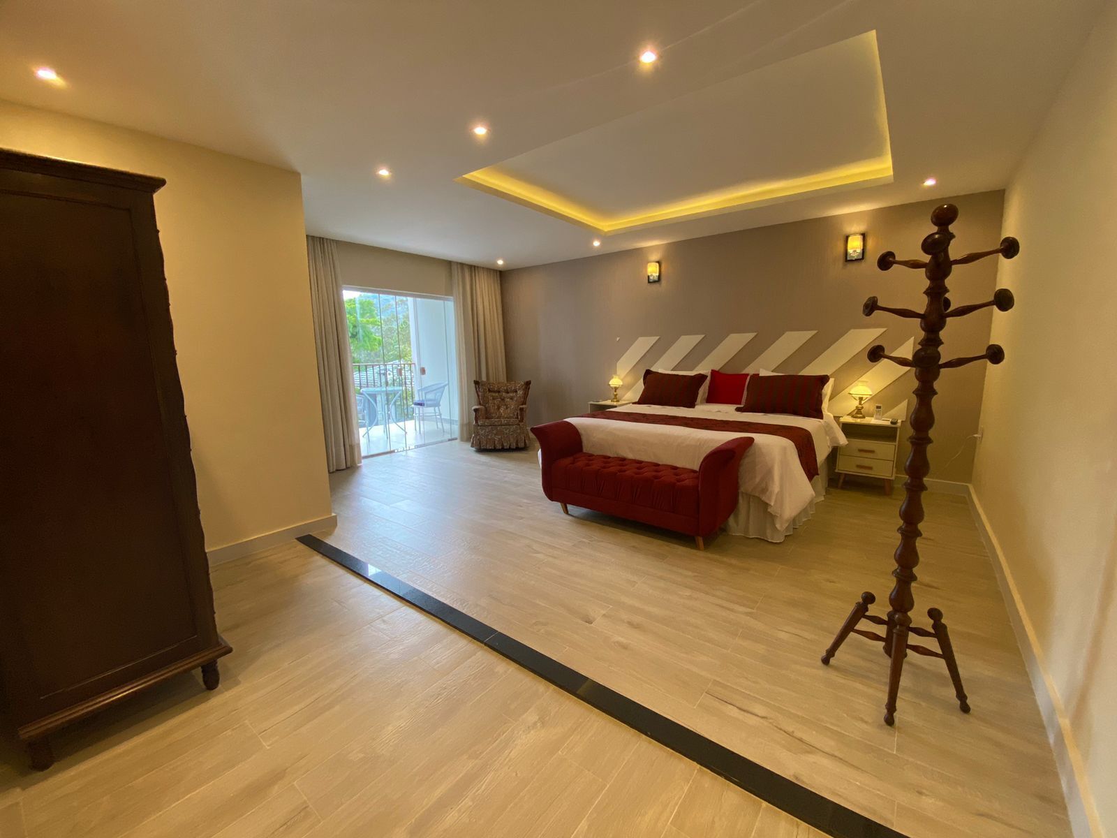 A modern bedroom with a large bed, a wooden wardrobe, and a balcony with a view.