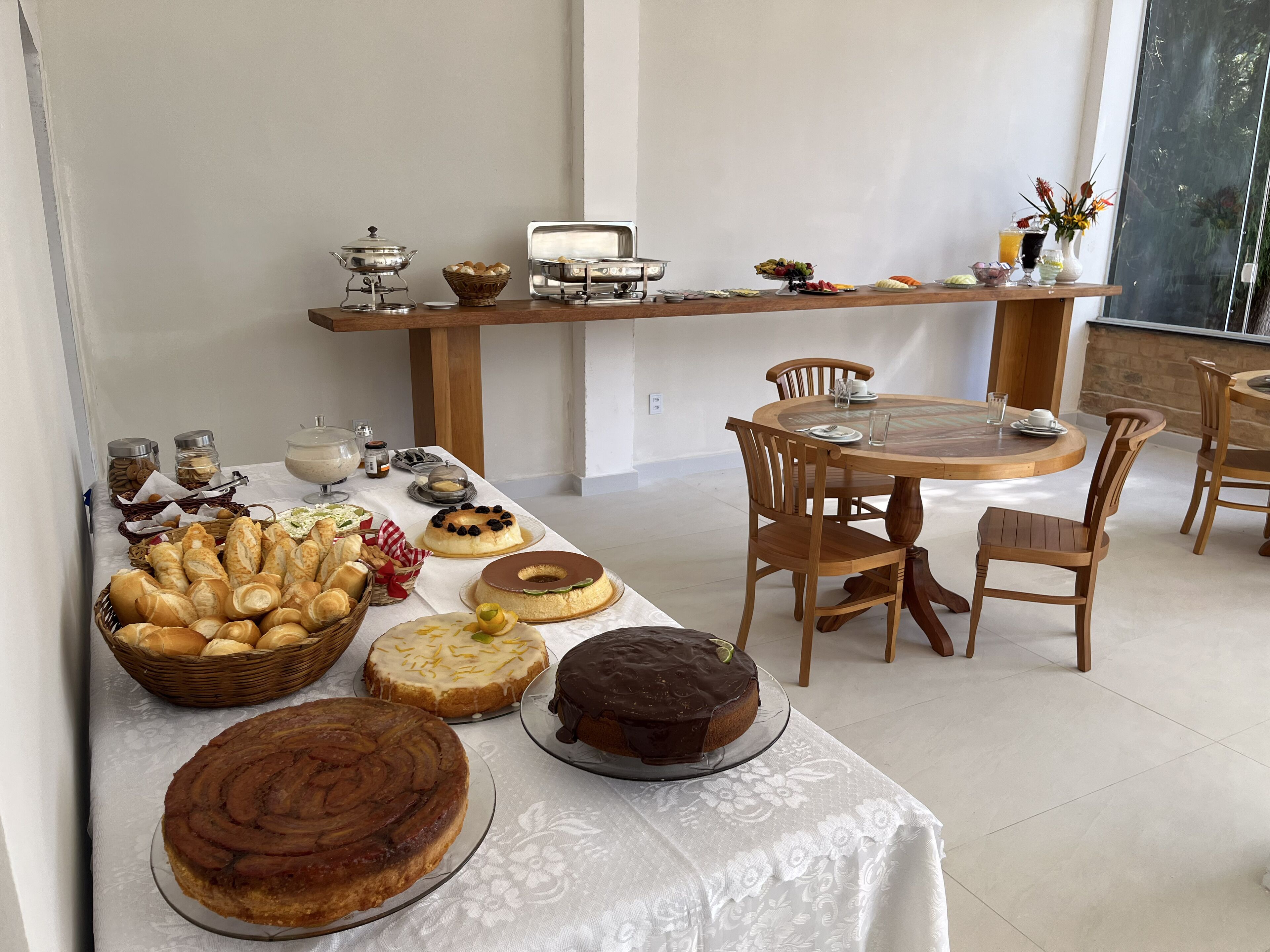 Un bufé de desayuno con diversos pasteles, tortas y bebidas sobre una mesa con sillas de madera.